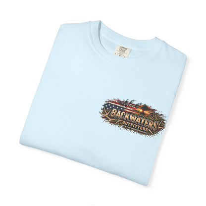 A light blue folded crewneck t-shirt with a 'Backwaters Outfitters' graphic printed on the left chest, displayed on a clean white background.